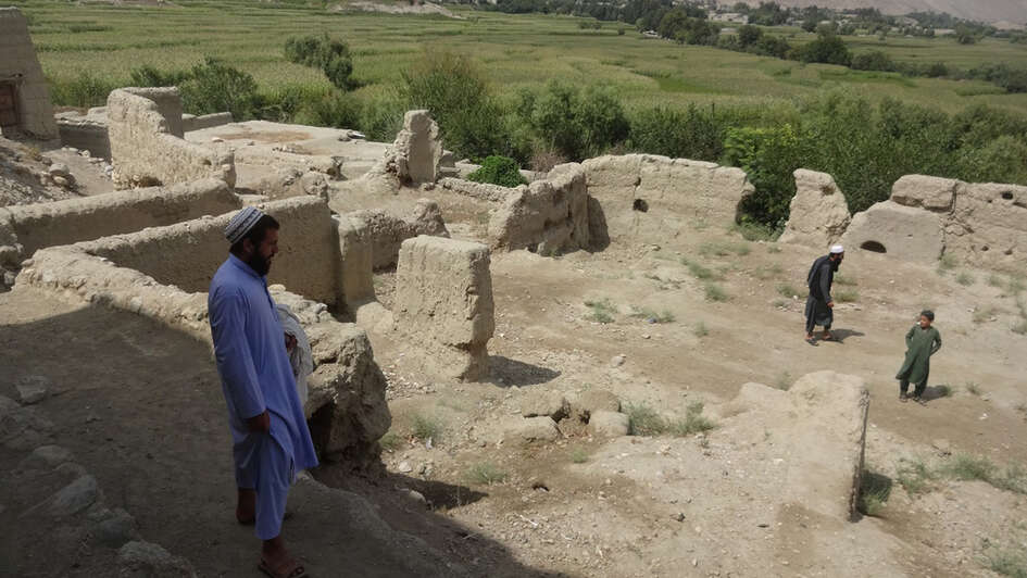 Ein Mann und zwei weitere Personen in weiterer Entfernung stehen in einer Ruine.