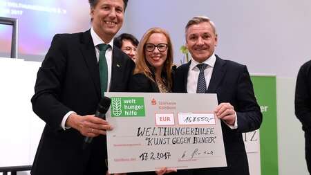 Vier Menschen mit einem großen Spendenscheck - der Erlös der Charity-Aktion Kunst gegen Hunger 2017.