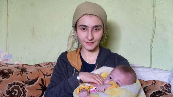 Eine Frau hält ein Baby im Arm und lächelt in die Kamera.