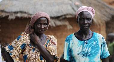 Zwei Kleinbäuerinnen in traditioneller Kleidung stehen vor einer Hütte in Burkina Faso