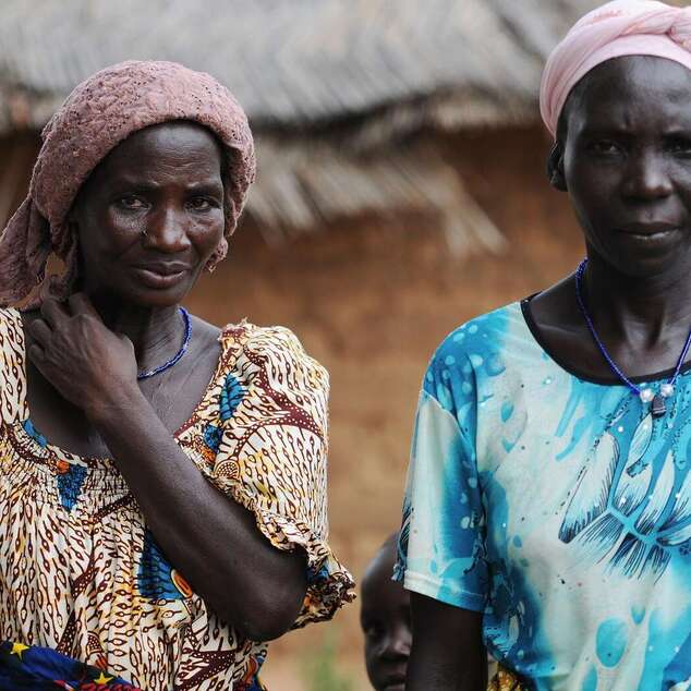 Zwei Kleinbäuerinnen in traditioneller Kleidung stehen vor einer Hütte in Burkina Faso