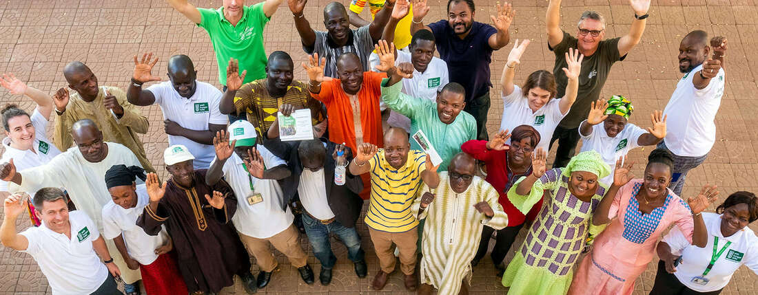 Eine Gruppe von Mitarbeiter*innen schaut Richtung Kamera und winkt