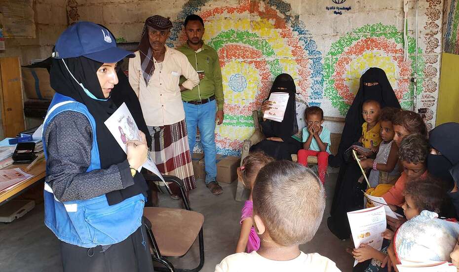 Eine Hilfsarbeiterin lehrt einer Gruppe Frauen und Kinder mithife einer Illustration Grundlagen über gesunde Ernährung.