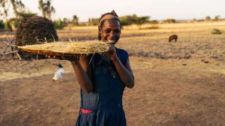 Eine Frau hält ein eine große Platte mit geerntetem Getreide in der Hand