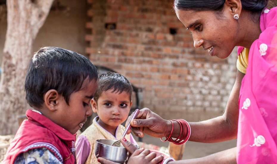 Eine Frau im Sari füttert einen kleinen Jungen.