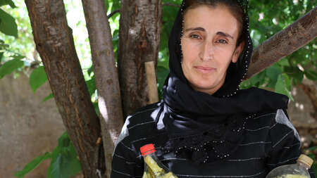 Eine Frau steht unter einem Baum, in der Hand hält sie zwei Flaschen mit Gewürzgurken, Türkei 2021.