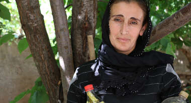 Eine Frau steht unter einem Baum, in der Hand hält sie zwei Flaschen mit Gewürzgurken, Türkei 2021.