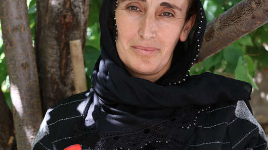 Eine Frau steht unter einem Baum, in der Hand hält sie zwei Flaschen mit Gewürzgurken, Türkei 2021.