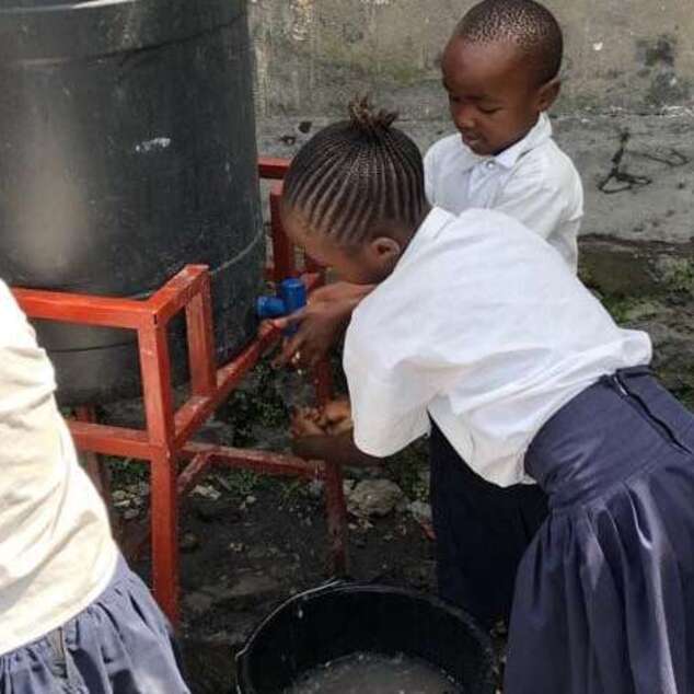 Schulkinder waschen sich an einem kleinen Wassertank die Hände.