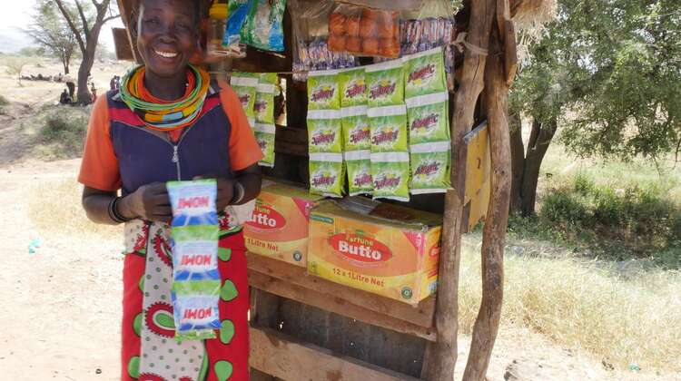 Eine Frau steht an einem kleinen Markstand und lächelt in die Kamera.