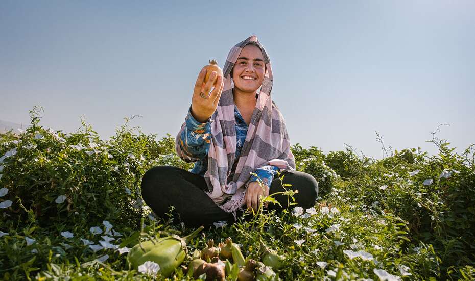 Frau sitzt im Feld und präsentiert stolz Früchte ihrer Ernte.