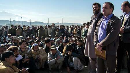 Flüchtlinge in Winterkleidung warten auf die Verteilung von Haushaltsgütern