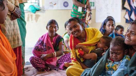 Frauen sitzen im Kreis und unterhalten sich. Manche haben Kinder auf dem Schoß.