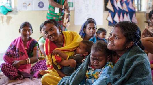 Frauen sitzen im Kreis und unterhalten sich. Manche haben Kinder auf dem Schoß.