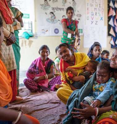 Frauen sitzen im Kreis und unterhalten sich. Manche haben Kinder auf dem Schoß.