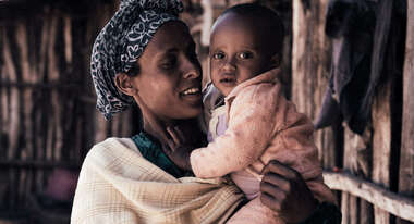 Eine Frau hält ein Baby im Arm und lächelt.