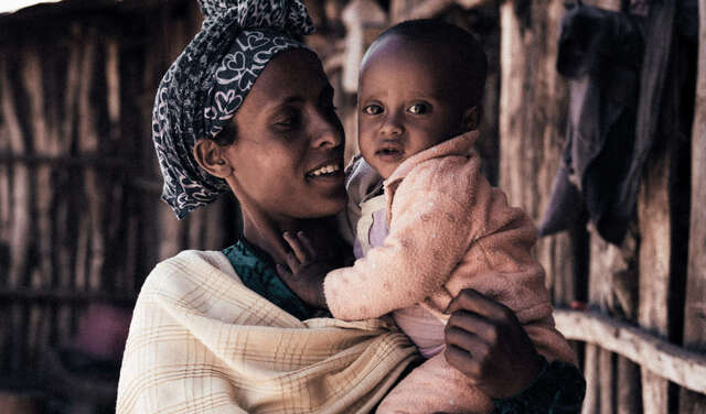 Eine Frau hält ein Baby im Arm und lächelt.