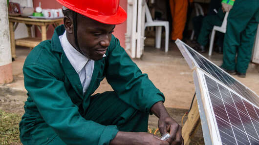 Der Auszubildende Cypriano Kwebiiha installiert eine Solaranlage.