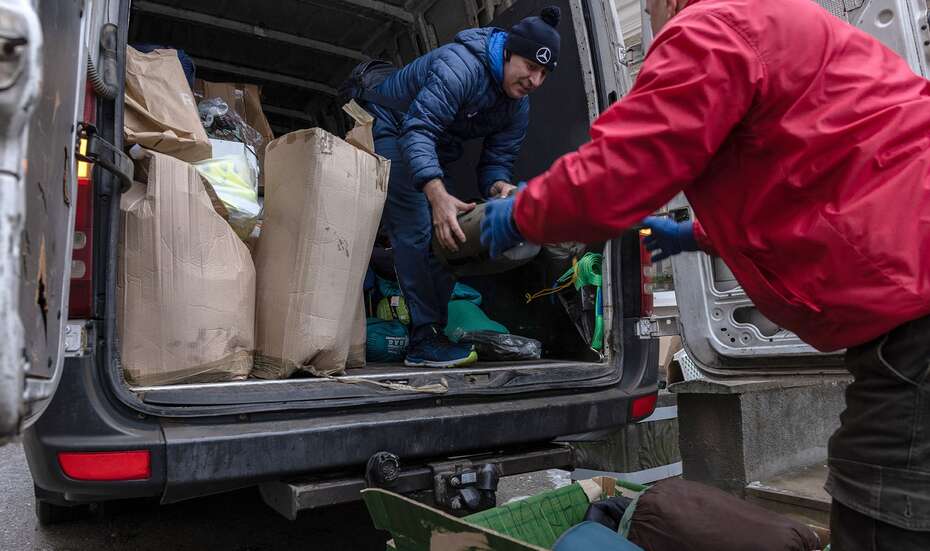 Zwei Personen in der ukrainischen Stadt Ternopil laden Hilfsgüter wie Kleidung und Decken aus einem Transporter.