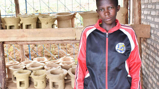 Eine junge Frau zeigt die neuen, effizienten Öfen, die sie baut, Burundi 2021.