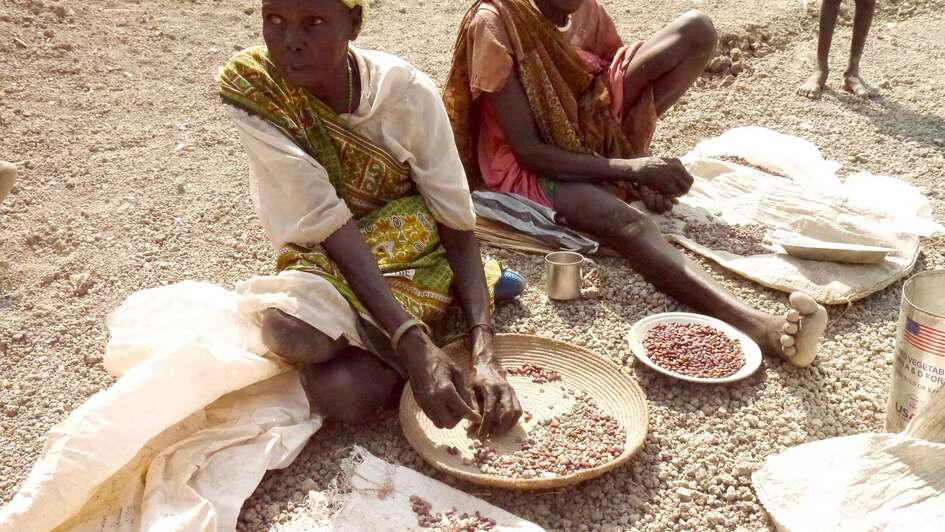 Zwei Südsudanesische Frauen sitzen auf dem Boden und bearbeiten Nahrung.