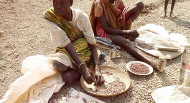 Zwei Südsudanesische Frauen sitzen auf dem Boden und bearbeiten Nahrung.