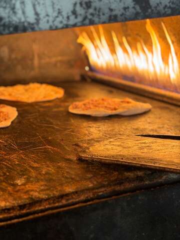 Ein befeuerter Backofen mit mehreren flach ausgerollten Laiben Brot.