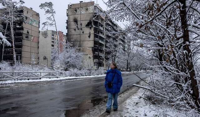 Eine Frau läuft eine Straße entlang, im Hintergrund zerstörte Wohnhäuser, es ist kalt und verschneit