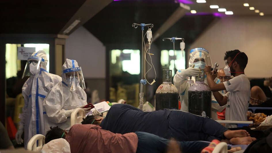 Drei Menschen in Schutzausrüstung kümmern sich um Menschen auf Krankenhaus-Liegen.