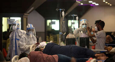 Drei Menschen in Schutzausrüstung kümmern sich um Menschen auf Krankenhaus-Liegen.