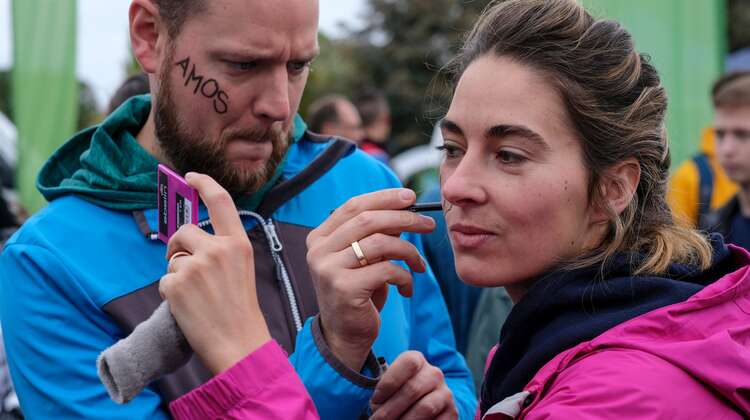 Eine Frau und eine Mann bemalen sich ihre Wangen.