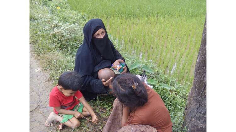 Flucht der Rohingya 3 Zwei Frauen mit Baby und Kind sitzen am Straßenrand.