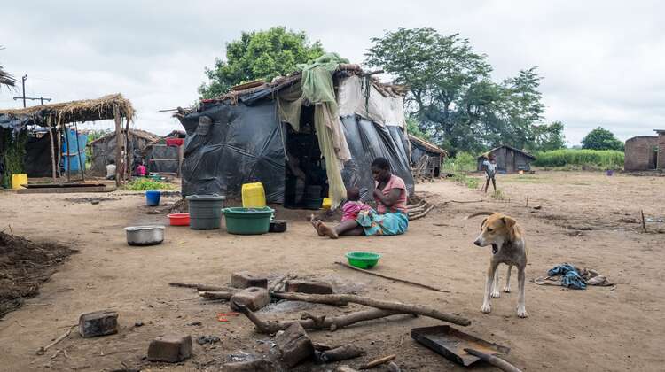 Eine Frau sitzt mit ihrem Kind auf dem Boden vor einer Hütte, die aus Planen und Decken gebaut wurde.