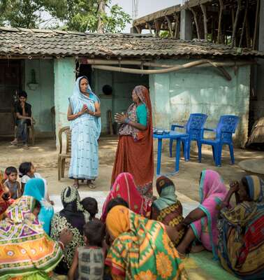 Mehrere Frauen sitzen im Halbkreis um zwei stehende Frauen, die etwas erklären.