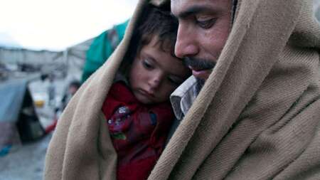 Vater sitzt mit Sohn zusammen in Decke eingehüllt im Flüchtlingscamp.