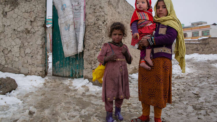 Zwei Mädchen stehen im Schneematsch, eine hält ein Baby auf dem Arm.