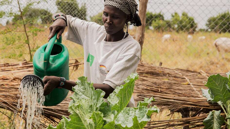 Eine Frau mit Giesskanne im Garten, Südsudan, 2017.