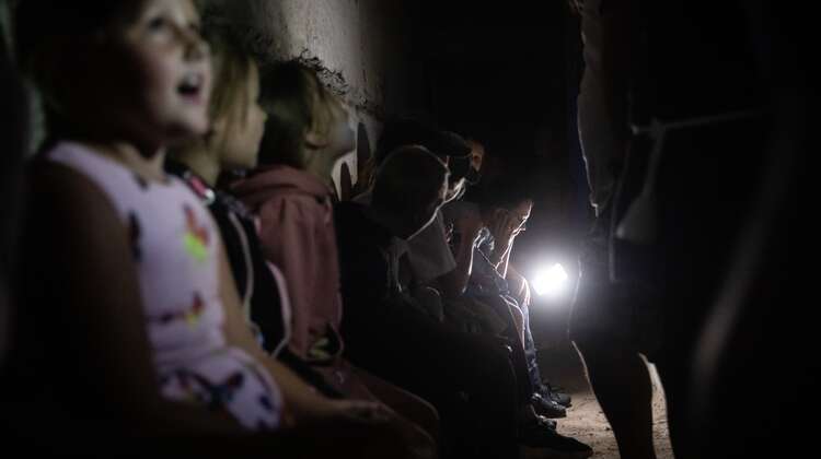 Ukrainische Kinder in einem Bunker, im Hintergrund leuchtet eine Taschenlampe