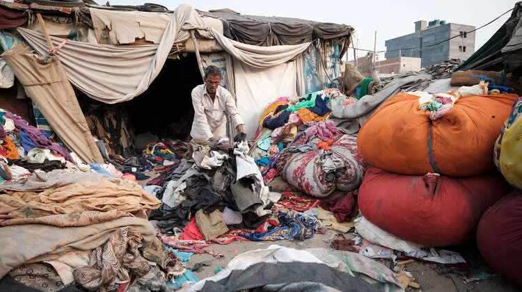 Ein Mann umgeben von Kleidungsstücken und alten Matratzen. Er sortiert Kleidung.