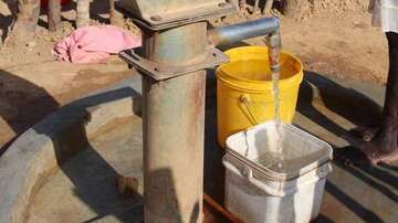 Ein Brunnen, aus welchem Wasser in einen Eimer läuft