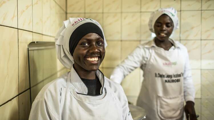 Eine junge Frau mit einer Koch-Haube lächelt in die Kamera.