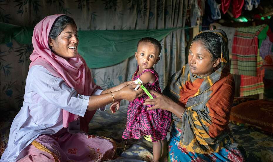 Eine Frau zu Besuch bei einem Kind und seiner Mutter, Kontrolle des Wachstums des Kindes durch Messung des Armumfangs
