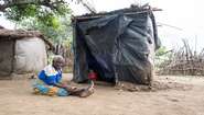 Eine ältere Frau sitzt auf dem Boden, hinter ihr eine Hütte aus Planen.