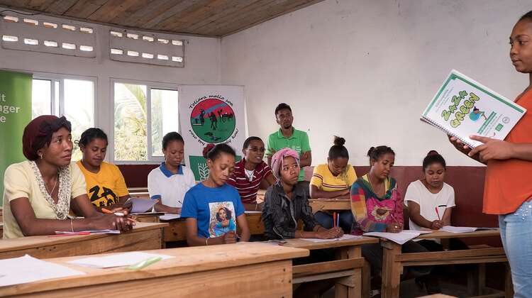 Eine Gruppe erwachsener Menschen sitzt auf Schulbänken bei einer Fortbildung zum Thema Müllmanagement.