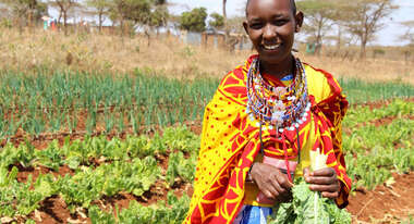 Eine Frau steht mit ihrer Ernte auf dem Feld, Kenia 2020. 