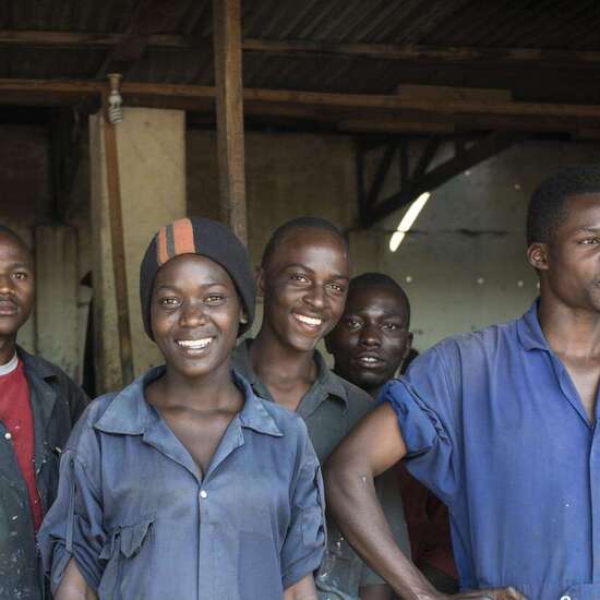 Jetzt als Unternehmen helfen. Bildbeschreibung: Eine Gruppe Jugendlicher in einer Autowerkstatt.