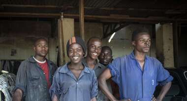 Jetzt als Unternehmen helfen. Bildbeschreibung: Eine Gruppe Jugendlicher in einer Autowerkstatt.