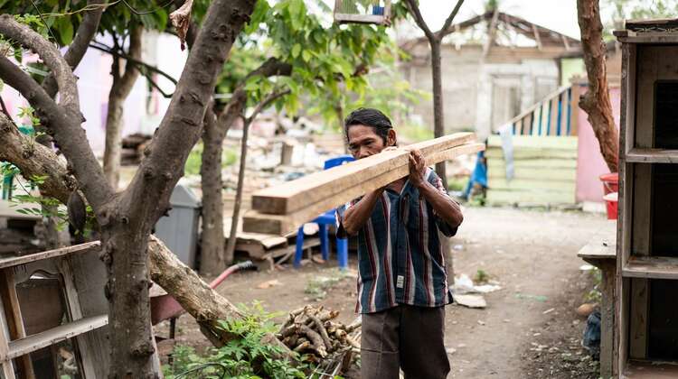 Ein Mann trägt zwei Holzlatten auf seiner Schulter.