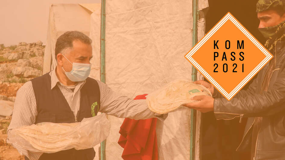 Ein Mann händigt einem anderen Mann eine Tüte mit Fladenbrot. Oben rechts ist das Kompass 2021 Logo.