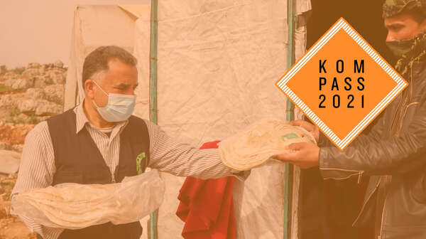 Ein Mann händigt einem anderen Mann eine Tüte mit Fladenbrot. Oben rechts ist das Kompass 2021 Logo.